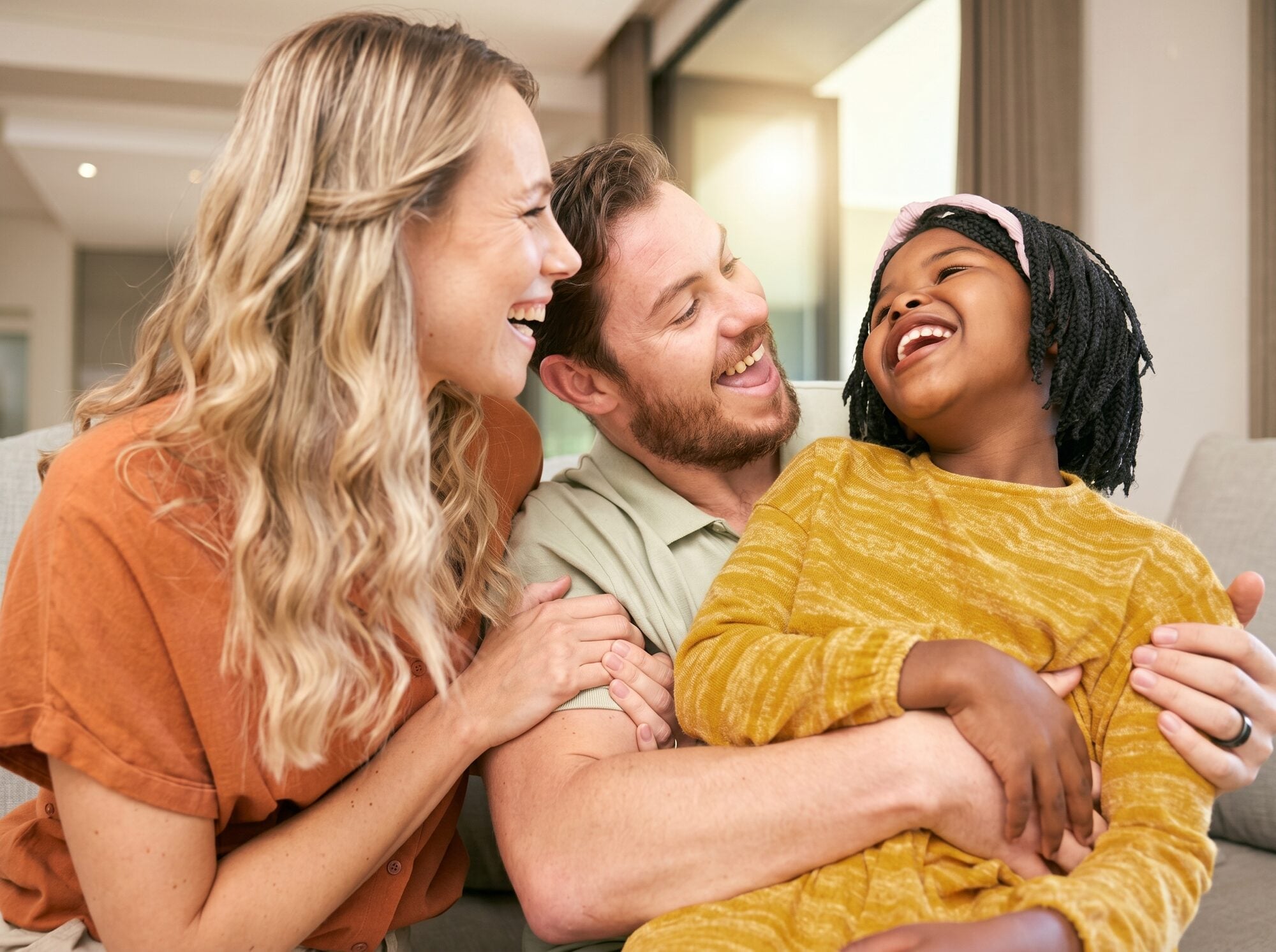A mother, father and young daughter laughing together on a sofa